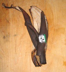 A blackened banana peel with a Fair Trade Certified sticker, lying on a wooden counter