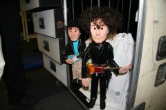 Marionettes of Beck and a bandmate hanging backstage beside road cases